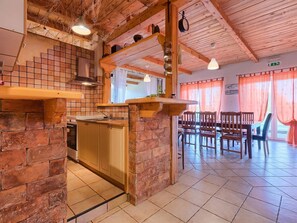 A rustic kitchen with a brick wall, wooden shelves, and a dining area with a table and chairs. - VILLA RENZO (Kaldanija)