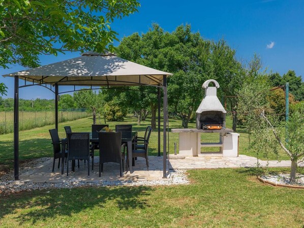 A covered outdoor dining area with a grill and chairs.
