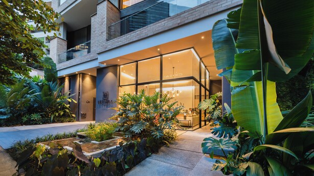 A modern building with a glass facade, a stone pathway, and lush tropical plants. - Lettera Hotel (Medellín)