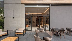 An outdoor patio with modern furniture, including sofas, chairs, and tables, and a glass door leading to an interior space. - Lettera Hotel (Medellín)