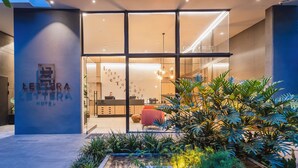 A modern hotel entrance with a glass facade, a reception desk, and a well-maintained garden area. - Lettera Hotel (Medellín)