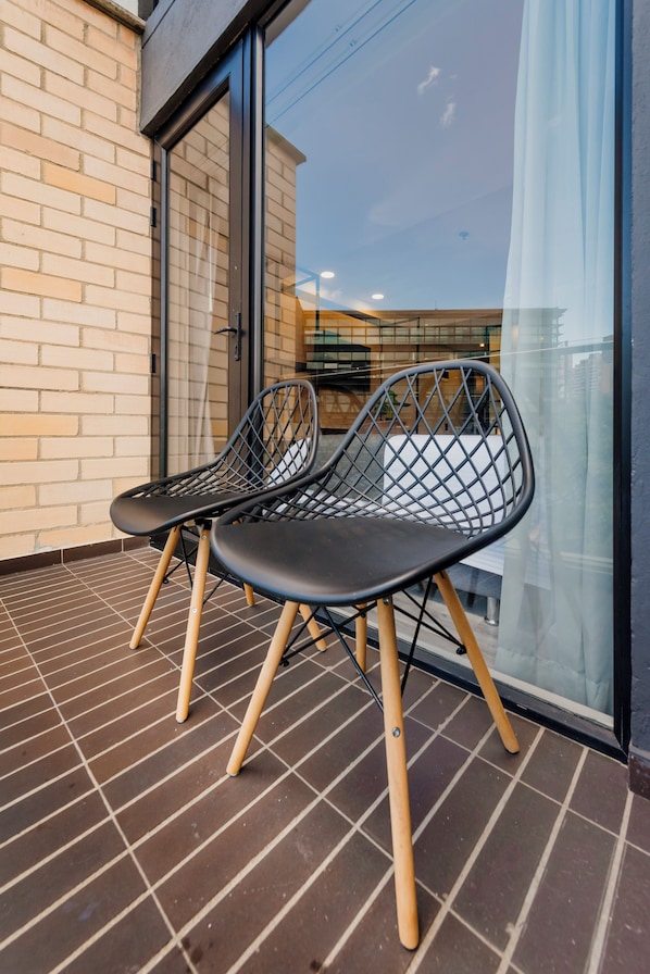 Two black mesh chairs with wooden legs on a tiled balcony with a glass door and a brick wall. - Lettera Hotel (Medellín)