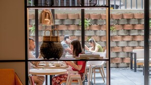 A café with round tables and chairs, a large woven basket centerpiece, and a brick wall background. - Lettera Hotel (Medellín)