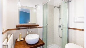 Une salle de bain moderne avec une douche à parois de verre, un meuble-lavabo en bois avec un lavabo blanc et un miroir au-dessus du lavabo.