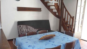 A dining area with a table set for four, a wooden bench, and a staircase. - House in Barbâtre on the Ile de Noirmoutier. Wifi La Cheminée 56 m2 -------- (Barbâtre)