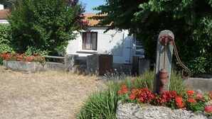 A rustic stone well with a metal pump, surrounded by red flowers and green plants, with a white building in the background. - House in Barbâtre on the Ile de Noirmoutier. Wifi La Cheminée 56 m2 -------- (Barbâtre)