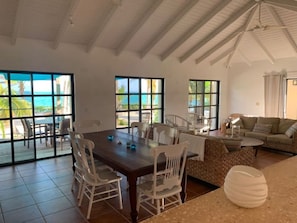 Enjoy ocean views from the large windows in this room, featuring a dining table, sofa, and small table with decorative item.