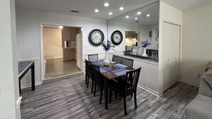 Un comedor con mesa y sillas de madera, un reloj en la pared y una cocina al fondo.