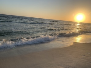 A beach with waves gently lapping at the shore and the sun setting in the background. - Family Ready: POOL :3BR/2BA Beach Cottage: Less than a block from Beach: WIFI (Panama City Beach)