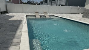Una piscina rectangular con agua cristalina, rodeada por un solárium con baldosas. Hay dos tumbonas mirando la piscina.