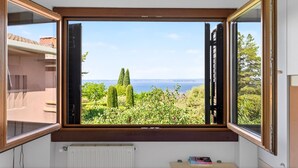 A room with a large window overlooking a garden and a body of water. - Regarda -Blue View 1  apartment with lake view, 1 bedroom, pool (Bardolino)