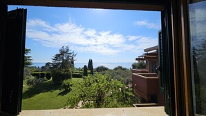 A view from a window overlooking a well-maintained garden with a clear sky and distant water body. - Regarda -Blue View 1  apartment with lake view, 1 bedroom, pool (Bardolino)