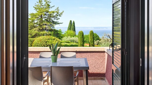An open balcony with a table and chairs, a potted plant, and a view of the sea and trees. - Regarda -Blue View 1  apartment with lake view, 1 bedroom, pool (Bardolino)