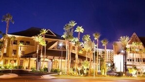 Un hotel con un diseño arquitectónico moderno, que destaca por un voladizo prominente y varias palmeras en primer plano.
