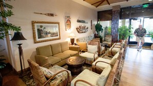 Un vestíbulo amplio con un sofá, sillas, una mesa de centro y una lámpara. Se observan elementos decorativos en las paredes y un gran ventanal con vistas.