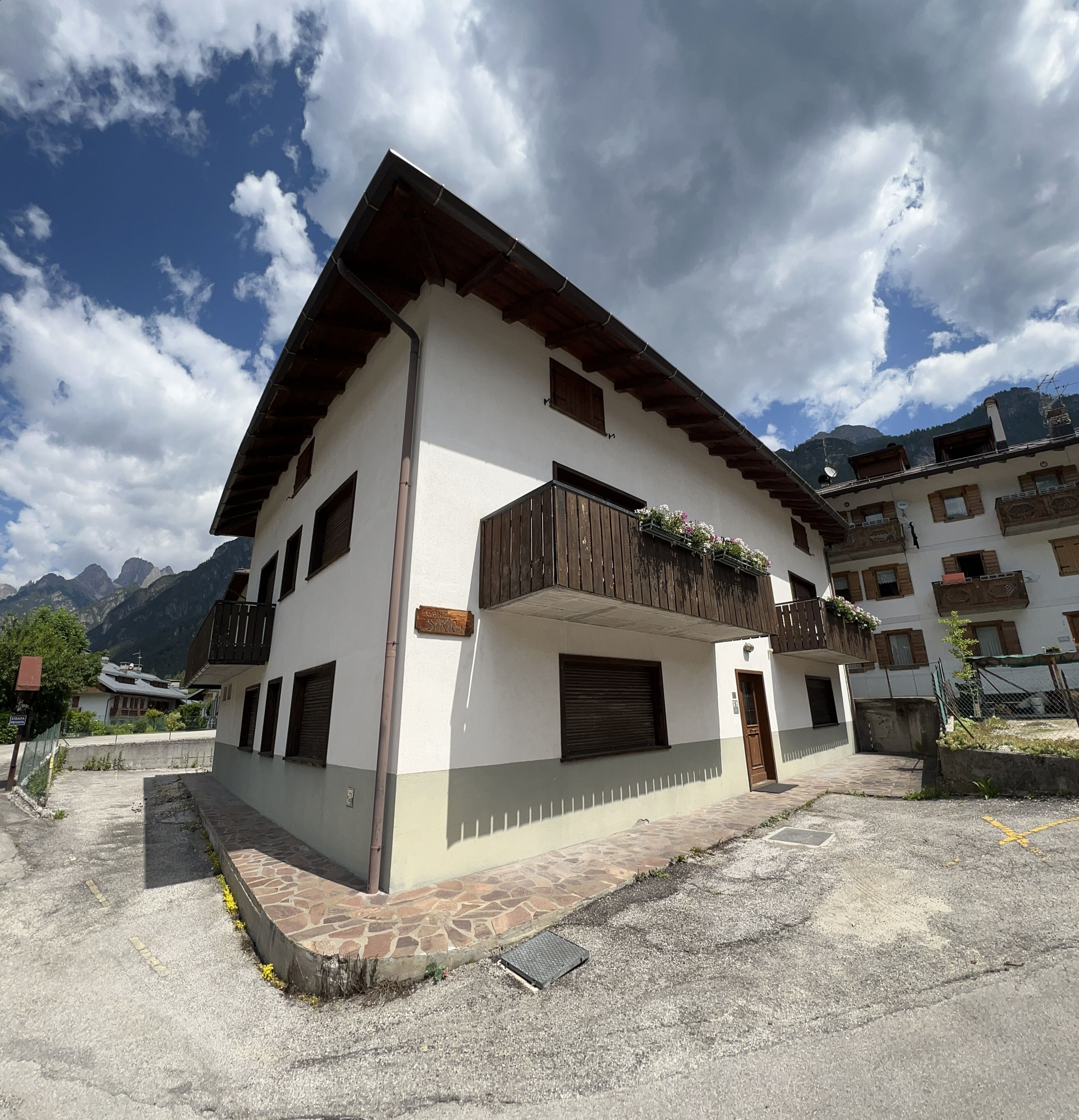 A two-story building with a white facade, wooden balconies, and a stone-paved entrance.