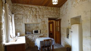 A stone-walled room with a wooden ceiling, a table with a checkered tablecloth, a microwave on a shelf, and a white refrigerator. - 3-Bedroom Stone House with a View (Nevşehir)