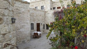 A courtyard with stone walls, a table with chairs, and a hanging plant. - 3-Bedroom Stone House with a View (Nevşehir)