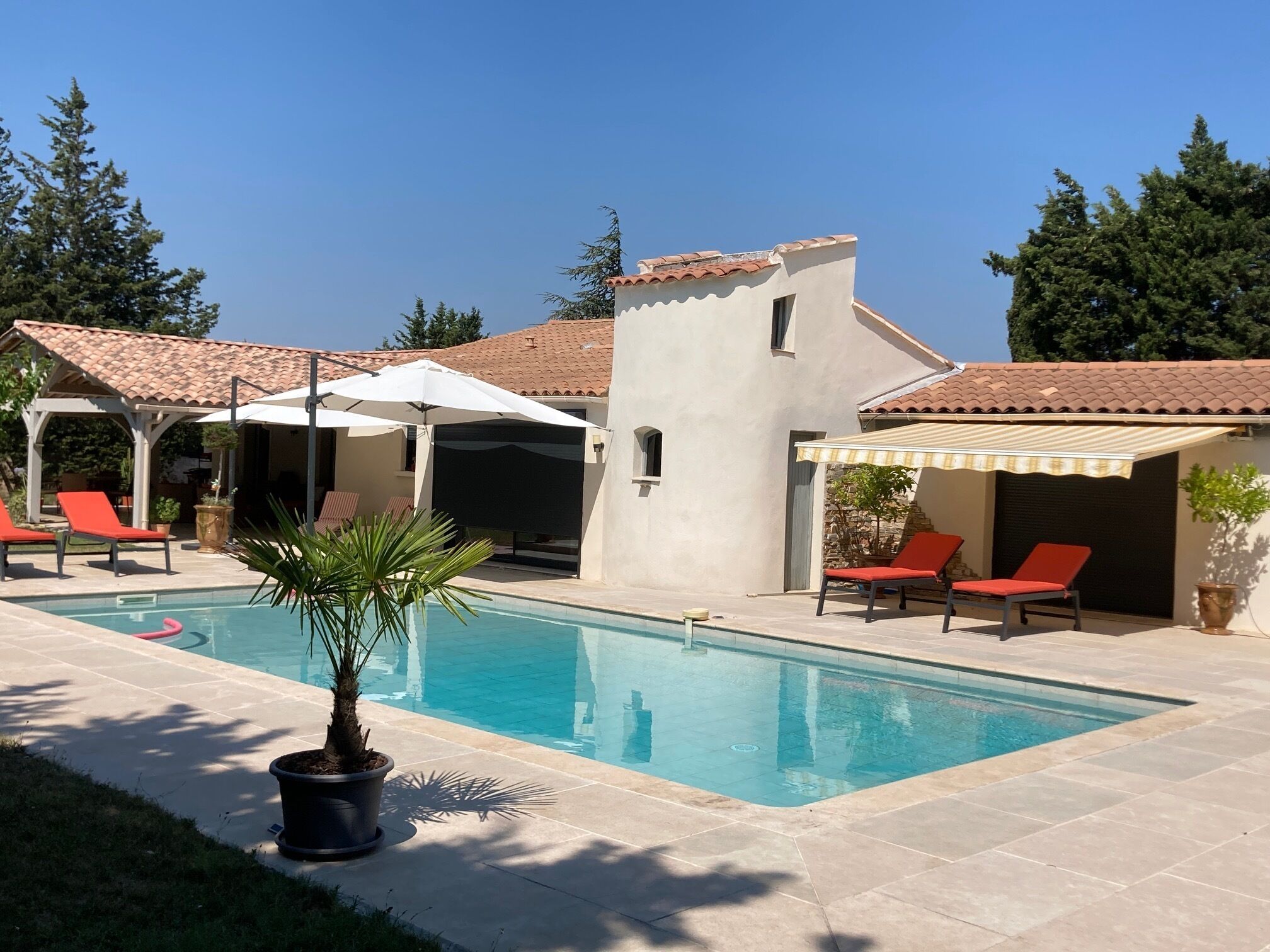 A swimming pool with lounge chairs and umbrellas, surrounded by a tiled patio and a stone wall.