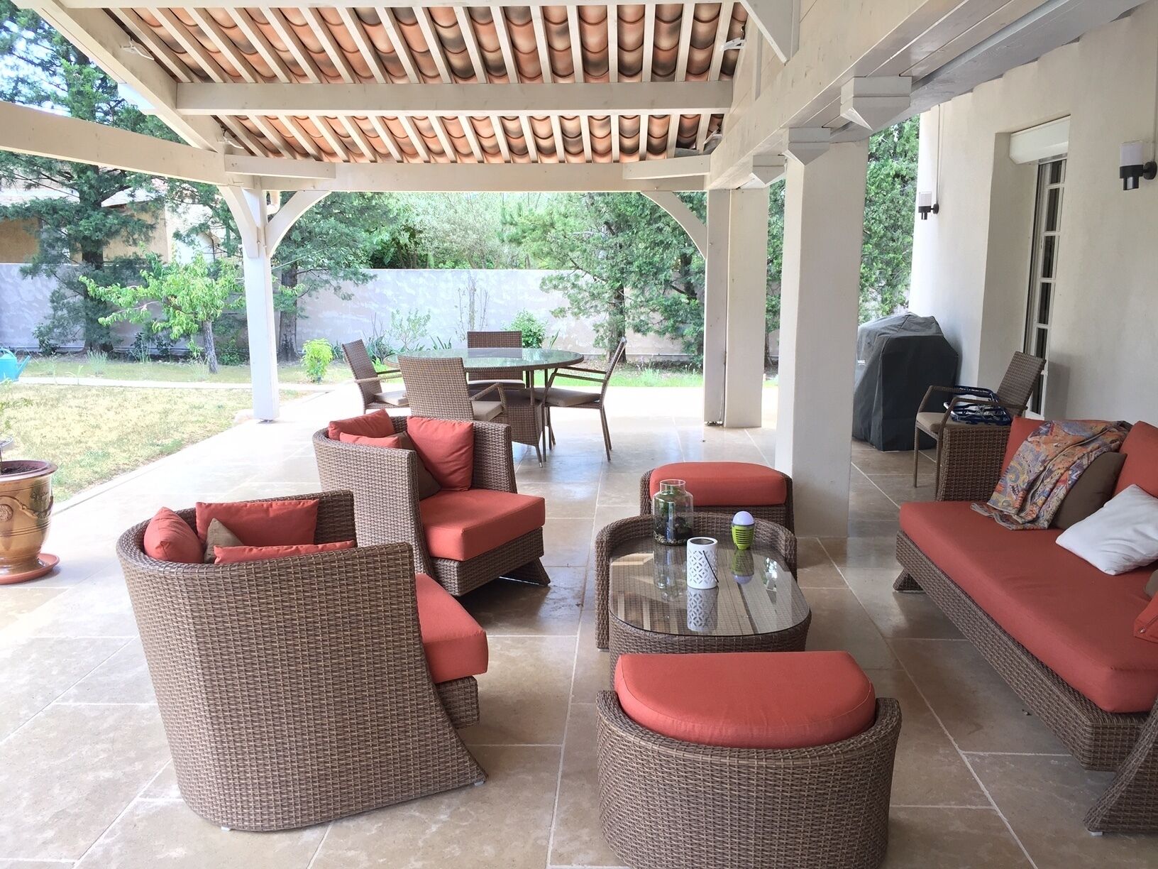 Eine Terrasse im Freien mit Korbmöbeln, einem Glastisch und einem roten Sofa.