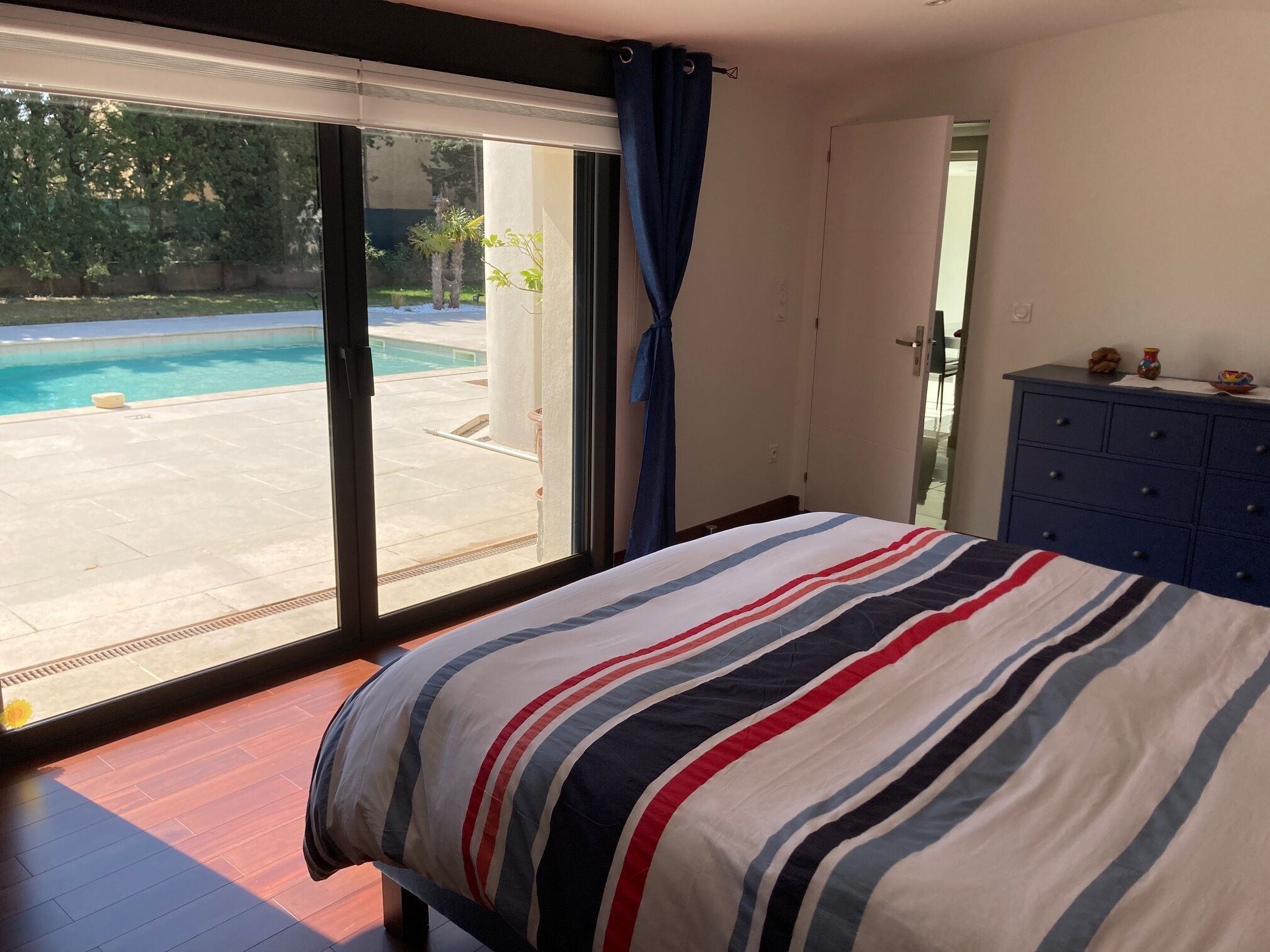 Quarto com cama, penteadeira e vista para uma piscina através de uma porta de correr.