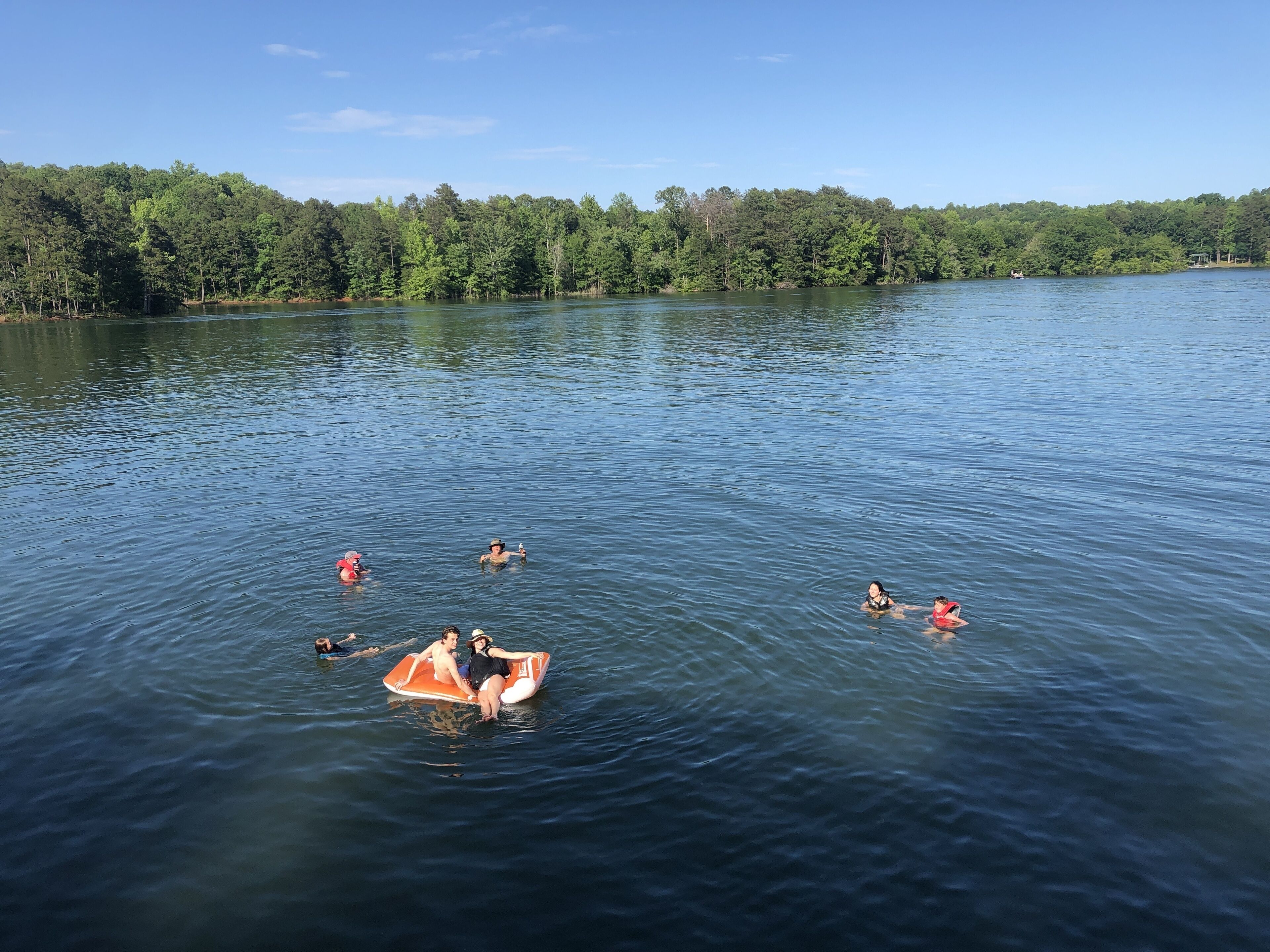 A calm lake with people floating on the water and a boat in the foreground.