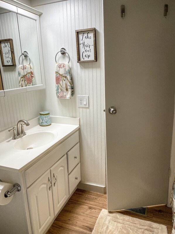 A bathroom with a white vanity, a sink, a mirror, and a door with a sign. - Deep Water Dock -two story! Bring your boat! Cozy pet friendly cottage (Fair Play)