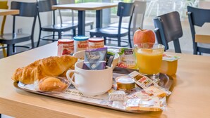 A breakfast tray with croissants, coffee, juice, and various packaged snacks on a table in a bright dining area with chairs and tables. - B&B HOTEL Marseille La Valentine (Marseille)
