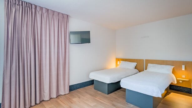 A hotel room with two single beds, a flat-screen TV, and a large window with curtains. - B&B HOTEL Marseille La Valentine (Marseille)