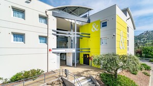 A modern hotel with a yellow and white facade, a visible entrance, and a staircase leading to the entrance. - B&B HOTEL Marseille La Valentine (Marseille)