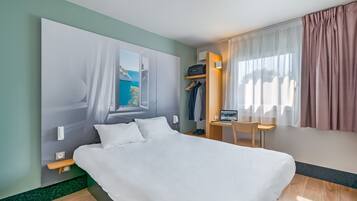 Une chambre d’hôtel moderne avec un grand lit, un bureau avec un ordinateur portable, une chaise et une vue sur la mer par la fenêtre.