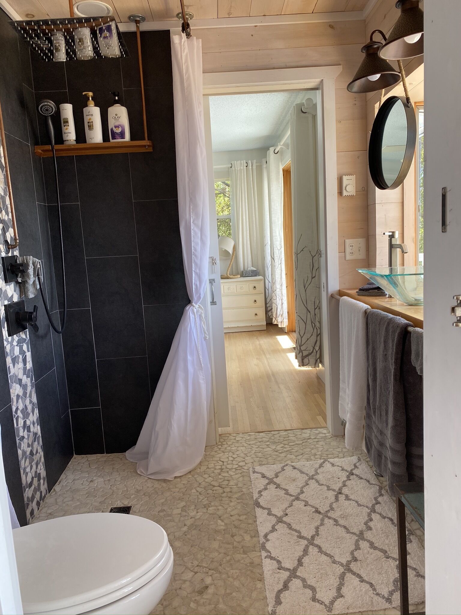 A bathroom with a shower, toilet, and sink. There are toiletries on a shelf and a towel rack.