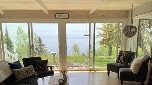 A spacious living room with a large window offering a view of the sea, a ceiling fan, and a sign reading "CabinHouse".