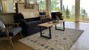 A cozy living room with a dark blue sofa, a wooden coffee table, and a view of trees outside.