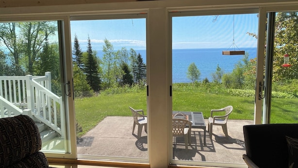 A cozy room with a large sliding glass door leading to a deck with outdoor furniture and a view of the ocean.