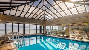 Ein überdachter Innenpool mit Glasdecke, großen Fenstern und Meerblick.