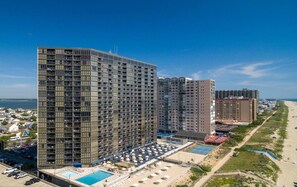 A high-rise hotel with multiple floors, a pool area, and a beach view.