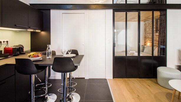 Une cuisine moderne avec un coin repas, un ensemble de tabourets de bar et un grand luminaire suspendu.