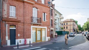 Une vue de rue avec un immeuble en briques rouges, un passage piéton et des voitures garées.