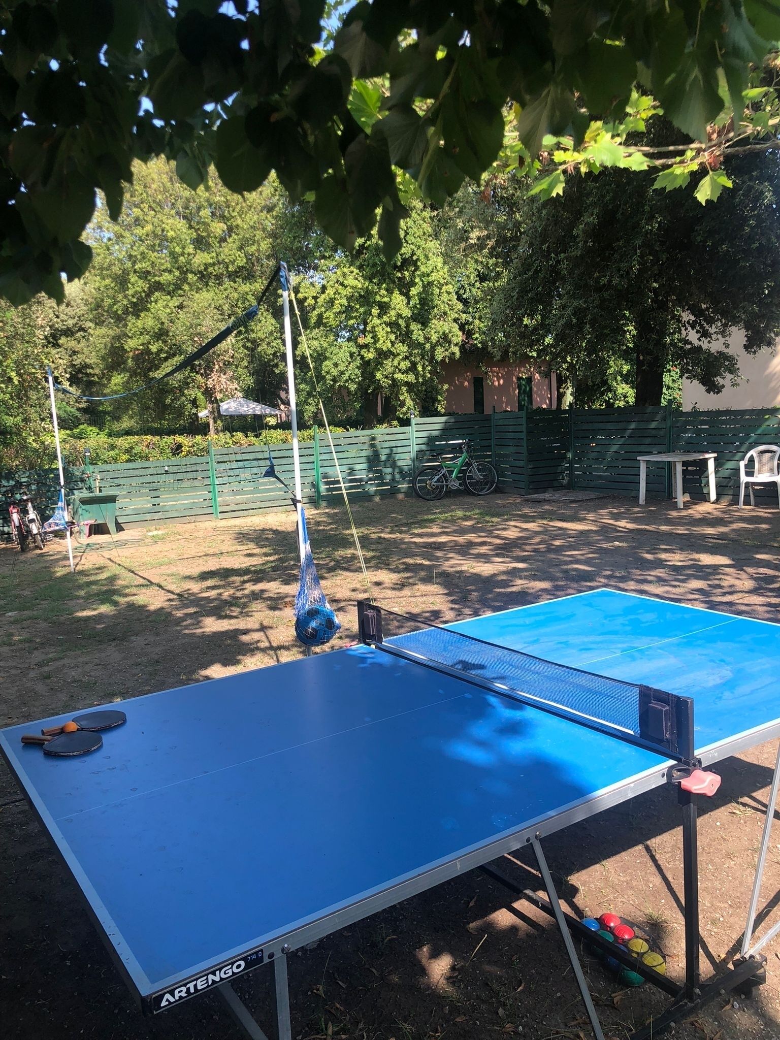An outdoor ping pong table with a net, a bicycle, and a table with chairs in a park.
