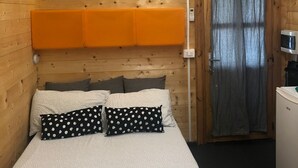 Une pièce de cabane en bois comprenant un lit, une petite kitchenette et une porte avec des rideaux.