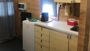 Une cuisine compacte avec des meubles en bois, un petit réfrigérateur, un évier et une fenêtre laissant entrer la lumière naturelle.
