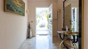 Un pasillo con piso de mármol, un cuadro en la pared, una mesa de vidrio con artículos de aseo y una puerta que da al exterior.