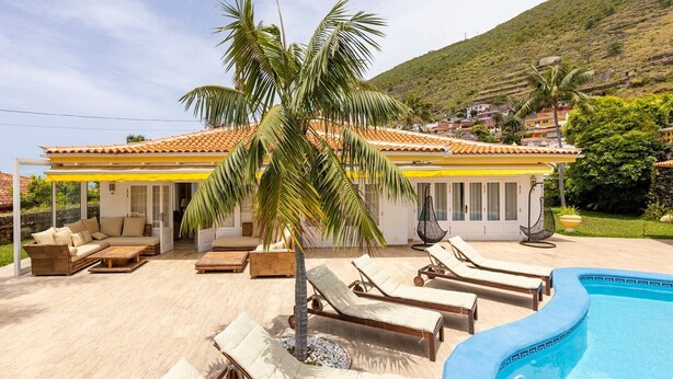Una villa con piscina, mobiliario exterior y vistas a una colina.