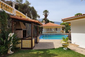 A pool area with a pergola, a statue, and a building with a tiled roof.