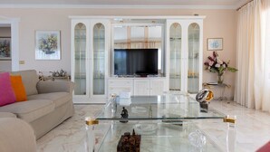 Una sala de estar con un sofá, una mesa de centro de vidrio, un televisor y un aparador con puertas de cristal.