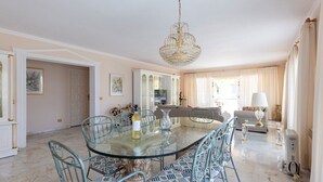 Un comedor amplio con una mesa y sillas de vidrio, una araña y vistas al salón.