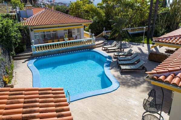 A swimming pool with a tiled deck, lounge chairs, and a building with a tiled roof.