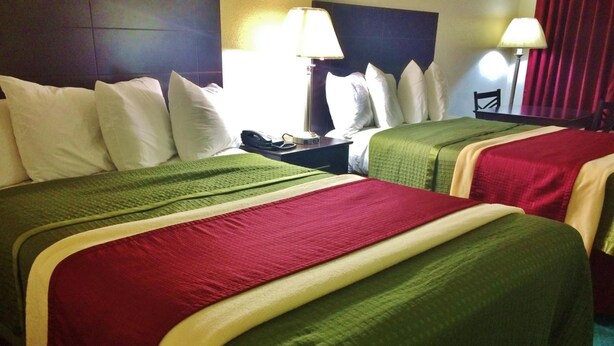A hotel room with two beds, each with a green and red bedspread, white pillows, and a nightstand with a lamp. - Travel Inn & Suites (Atlanta)