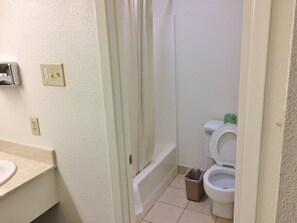 A bathroom with a toilet, a trash bin, and a bathtub.